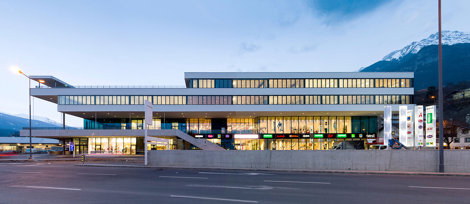Exterior view of the brightly illuminated building at dusk; the bottom two floors are a shopping center; the school floors are above.