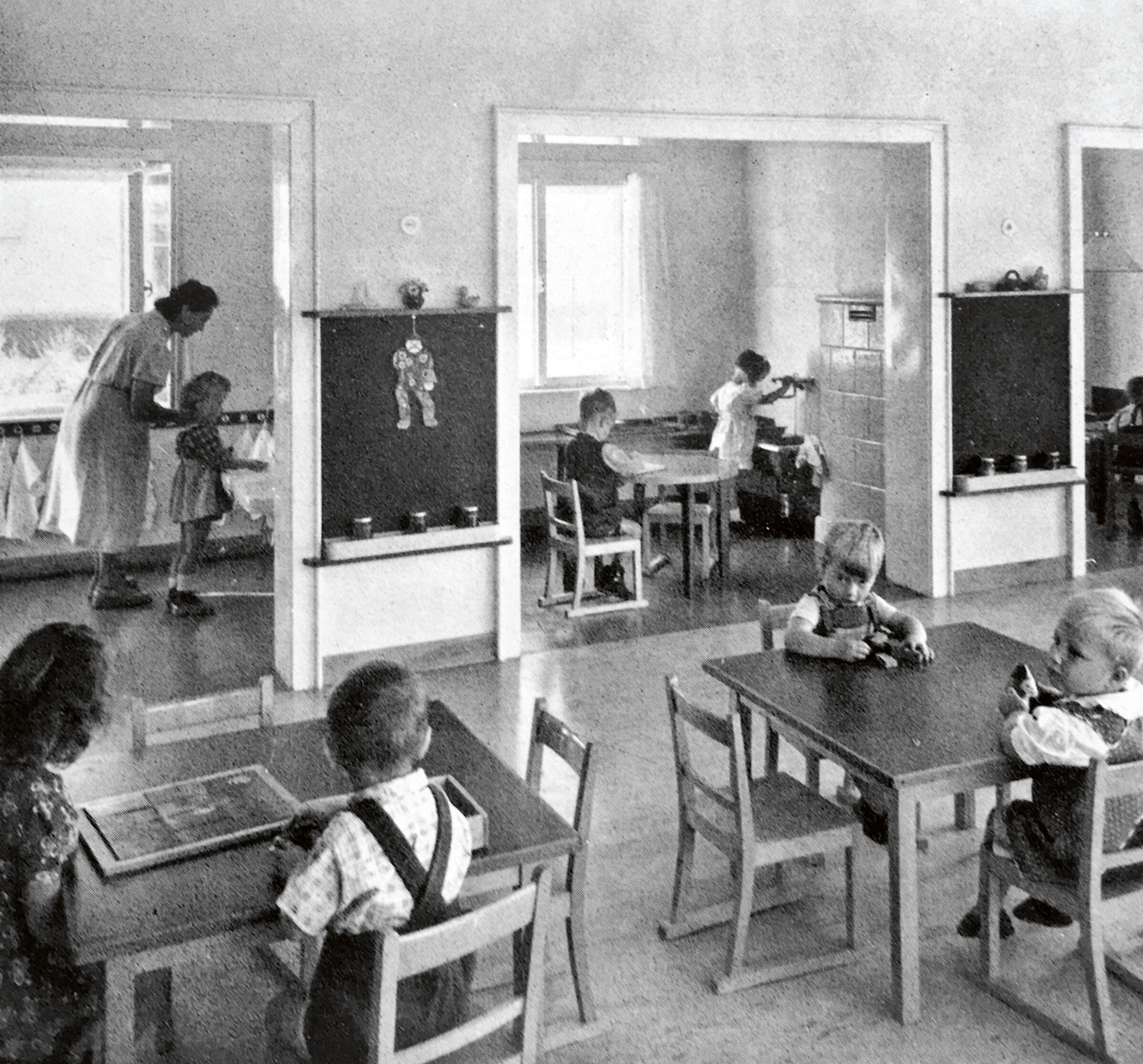 A black and white photo shows children seated at low tables.